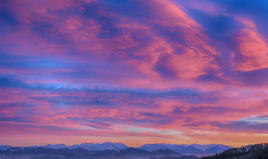 Vibrant purple and pink sunset clouds over snow-capped mountains