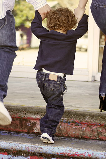 Toddler walking away holding parents hands on sidewalk
