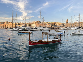 Traditional red wooden boat in a Mediterranean harbor with historic city skyline