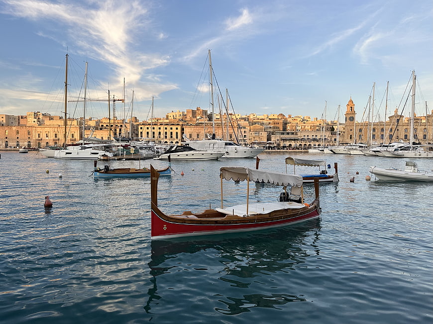 Traditional red wooden boat in a Mediterranean harbor with historic city skyline