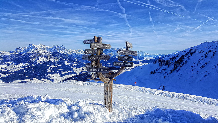 Wooden signpost with city distances in snowy alpine landscape