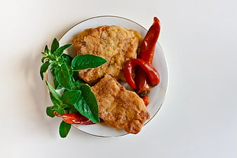 Fried fish fillets with red chili peppers and fresh herbs on white plate