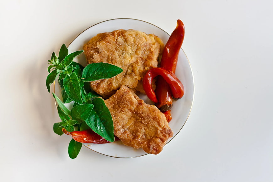 Fried fish fillets with red chili peppers and fresh herbs on white plate