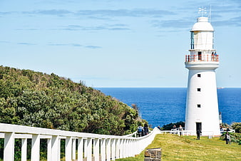 White Lighthouse on Coastal Cliff with Blue Ocean Background