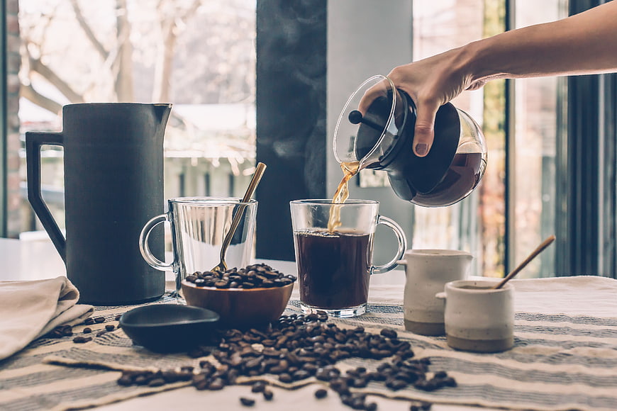 Pouring Fresh Coffee into Glass Mug with Beans