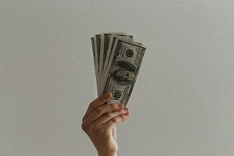Hand holding stack of hundred dollar bills on white background