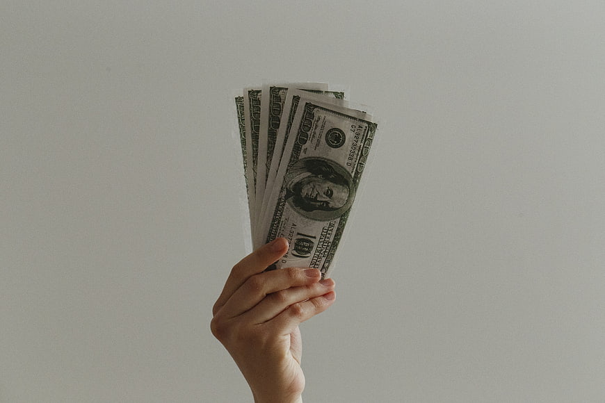 Hand holding stack of hundred dollar bills on white background
