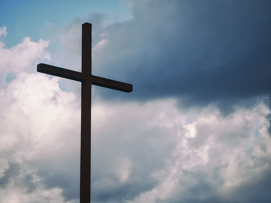 Silhouette of a wooden cross against a dramatic cloudy sky