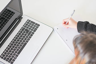 Overhead view of person writing in notebook next to laptop
