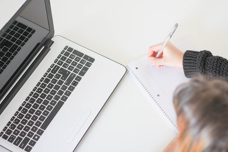 Overhead view of person writing in notebook next to laptop