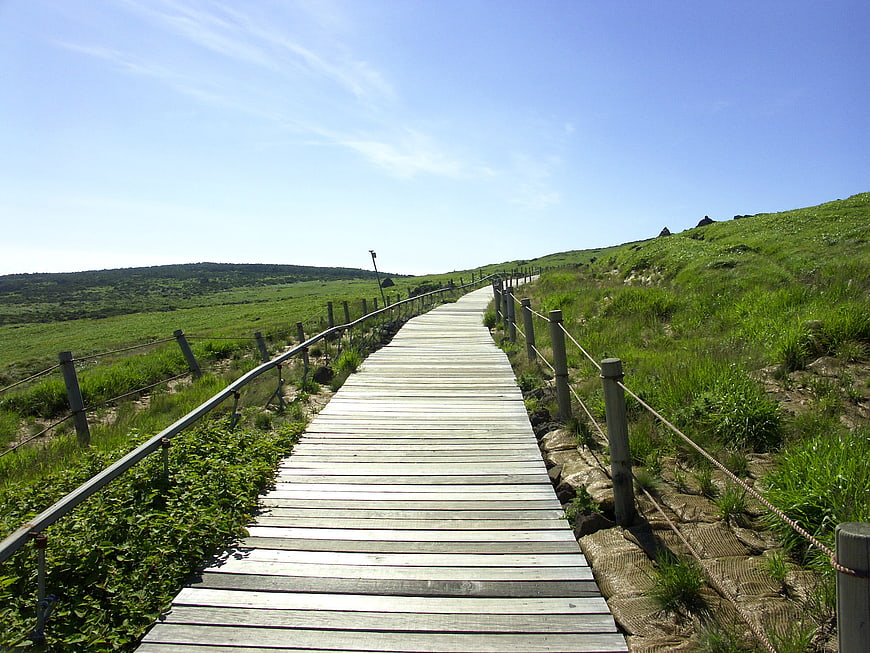 Wooden boardwalk path leading through green grassy hills under a clear blue sky
