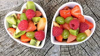 Heart-shaped bowls of fresh mixed fruit salad on rustic wood