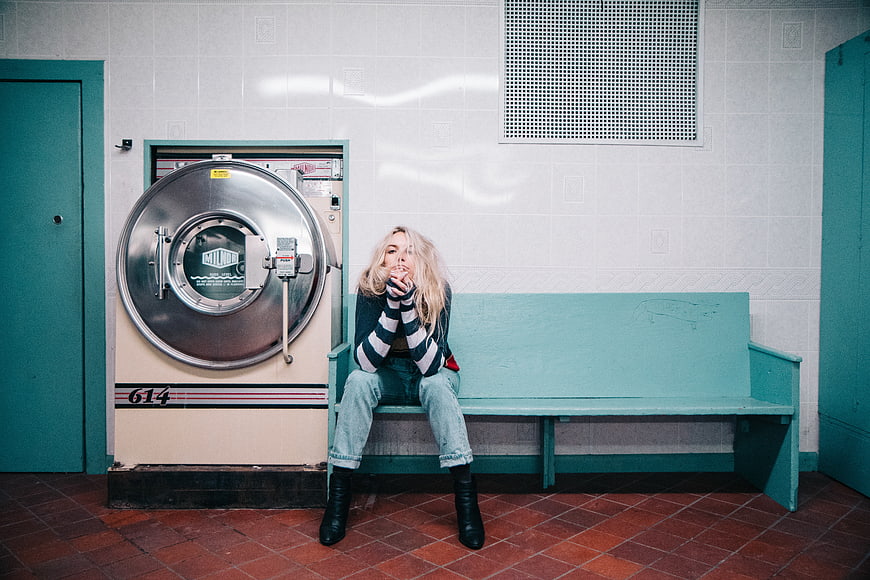 Blonde woman sitting on bench in retro laundromat