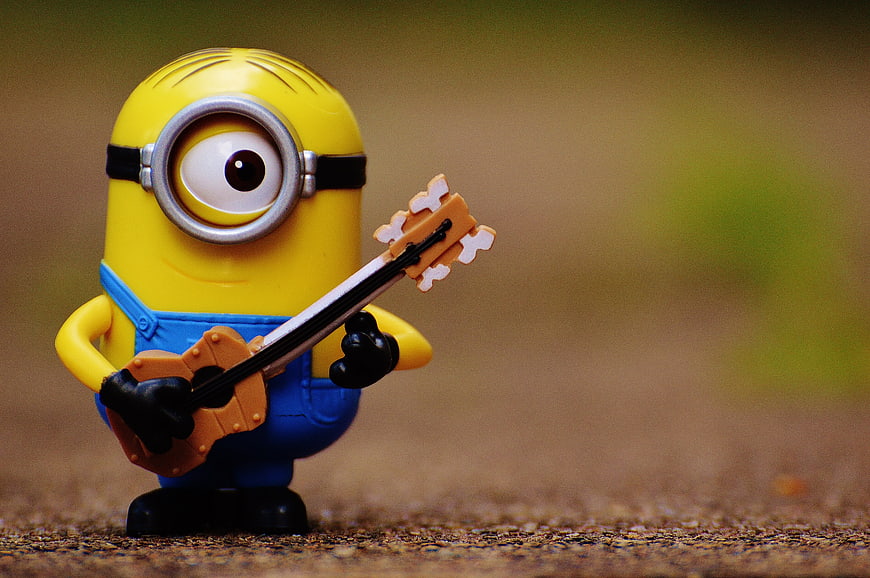 Cute Minion Toy Playing Guitar On Textured Ground