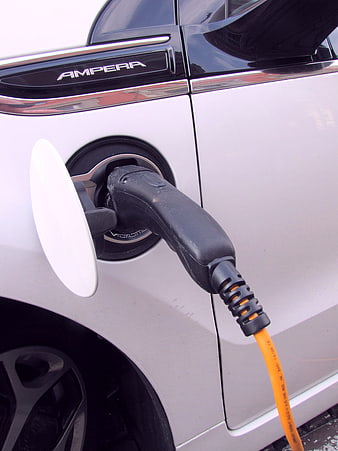 Close-up of white electric car charging with orange cable