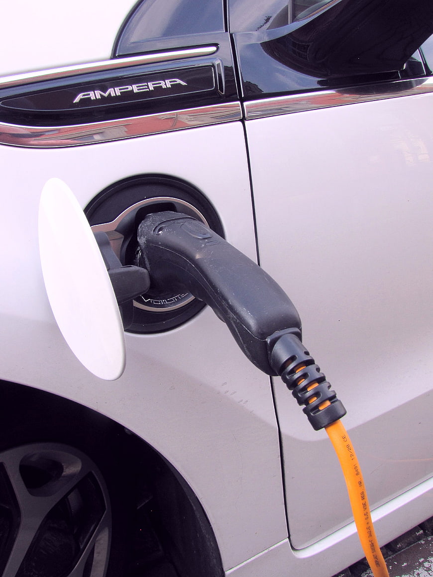Close-up of white electric car charging with orange cable