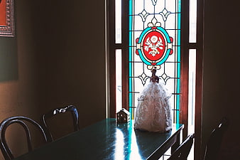 Vintage doll in lace dress on table by stained glass window