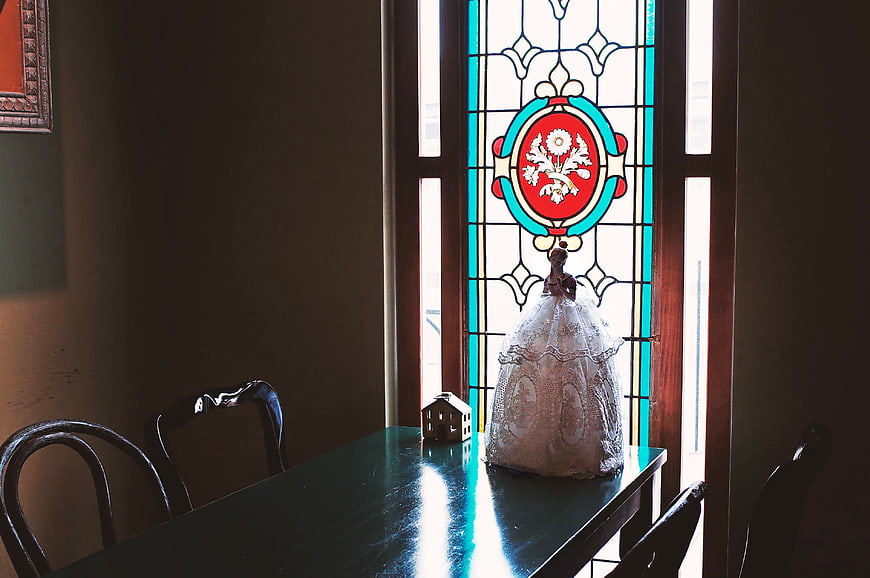 Vintage doll in lace dress on table by stained glass window