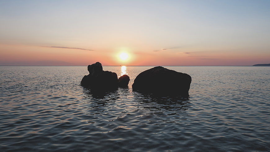 Silhouetted Rocks in Calm Ocean at Sunset