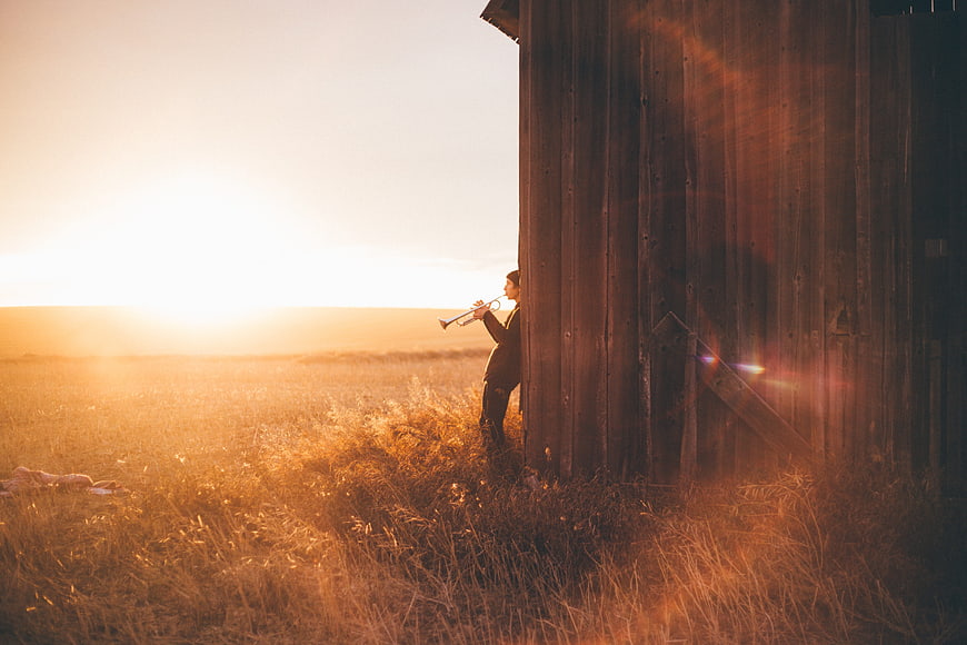 Man playing trumpet in field at sunset