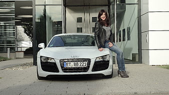 Woman in leather jacket leaning on white Audi R8 sports car