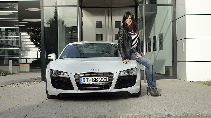 Woman in leather jacket leaning on white Audi R8 sports car