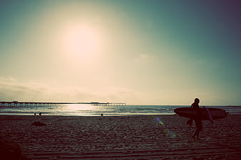 Silhouette of Surfer Walking on Beach at Sunset