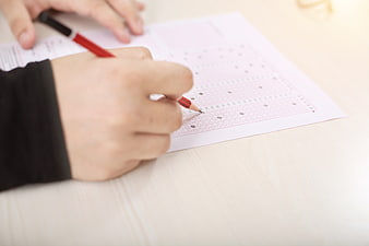 Close-up of hand filling out OMR exam sheet with red pencil