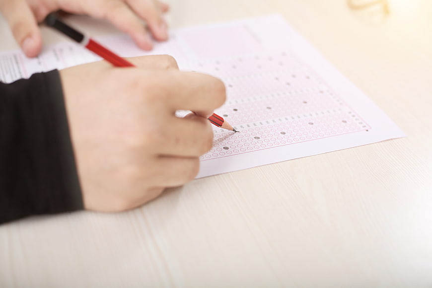 Close-up of hand filling out OMR exam sheet with red pencil