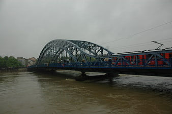 Red tram crossing blue steel bridge over flooded river
