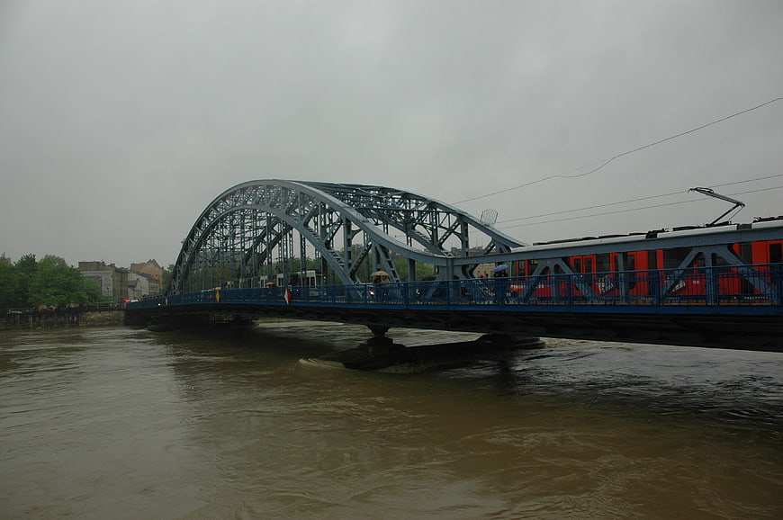 Red tram crossing blue steel bridge over flooded river