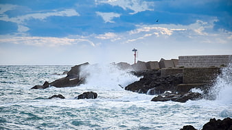 Powerful Waves Crashing Against Coastal Breakwater and Lighthouse