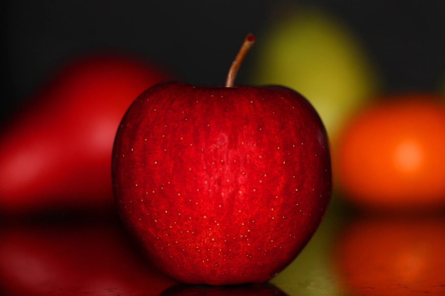 Close-up of a shiny red apple with blurred fruit background