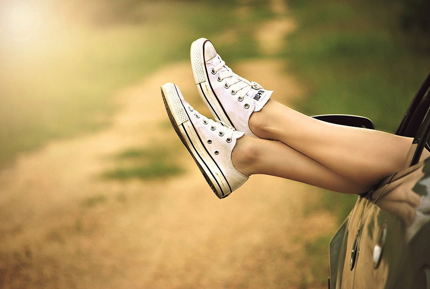 Woman's legs in white sneakers hanging out of car window