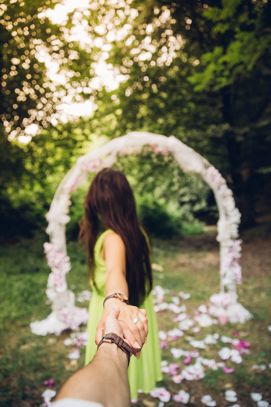 Woman in Green Dress Leading by Hand Towards Floral Arch