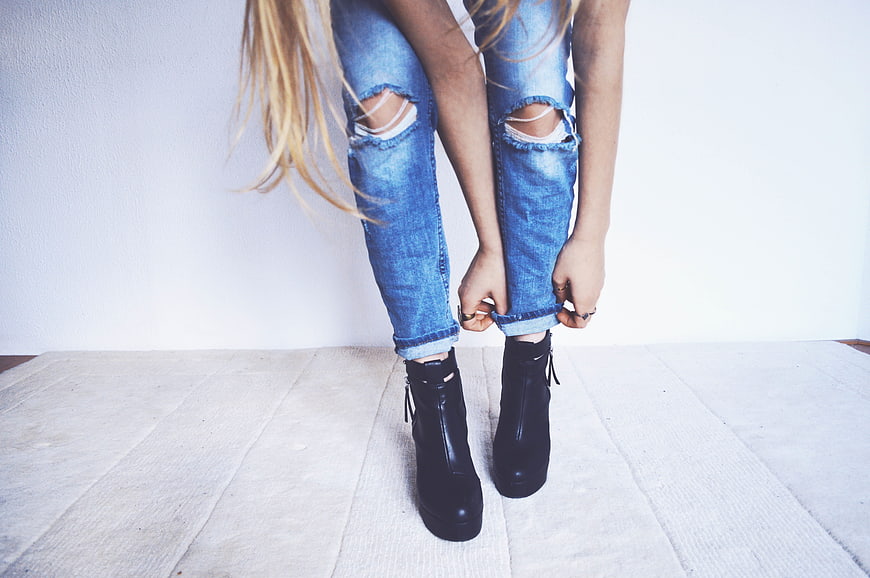 Woman rolling up ripped jeans with black boots