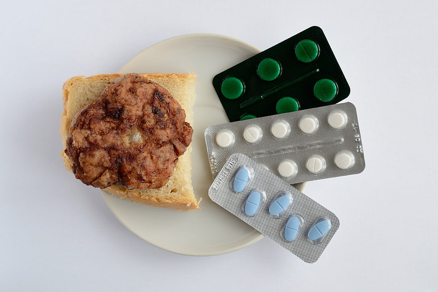 Flat lay of fried meat patty on bread with blister packs of pills