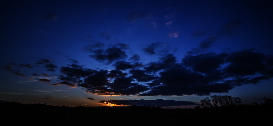 Dramatic blue dusk sky with sunset clouds over silhouette landscape