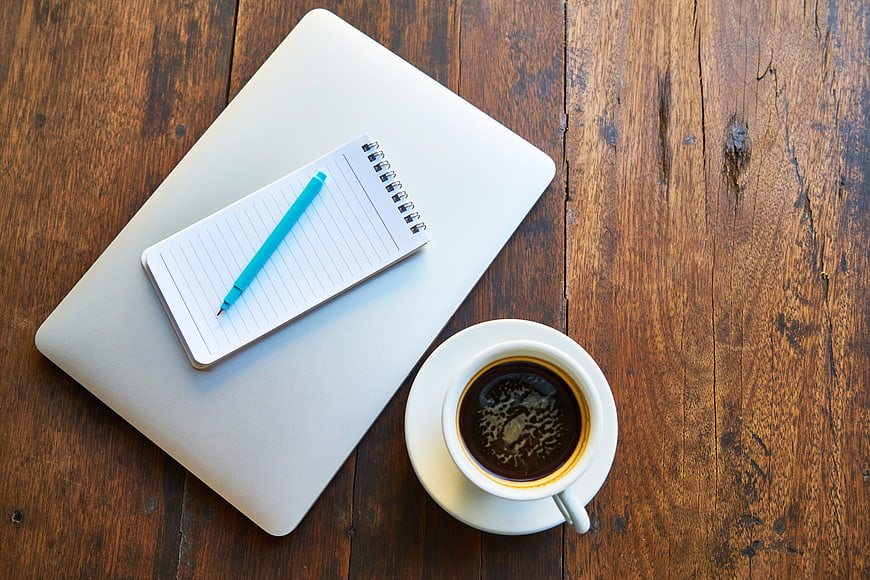 Flat lay workspace with laptop, notebook, pen, and coffee on wood