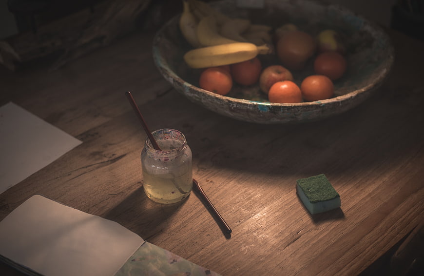 Still life of paint jar, brush, and fruit bowl on wooden table