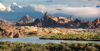 Dramatic Red Rock Mountains Beside River and Green Vegetation