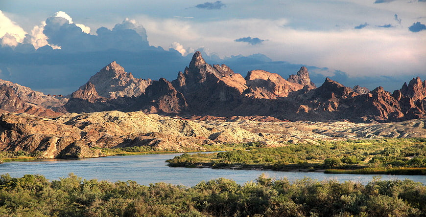 Dramatic Red Rock Mountains Beside River and Green Vegetation