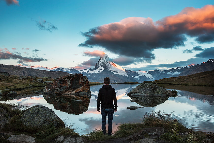 Man standing by lake viewing Matterhorn mountain at sunset