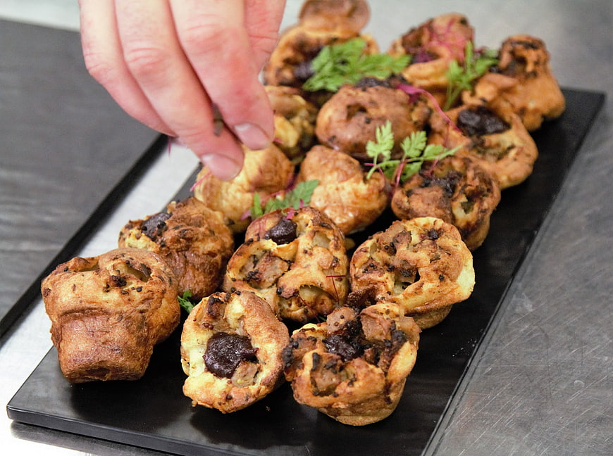 Chef garnishing savory Yorkshire puddings on black slate platter