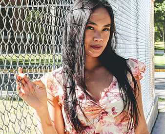 Young Woman in Floral Dress Leaning Against Chain Link Fence
