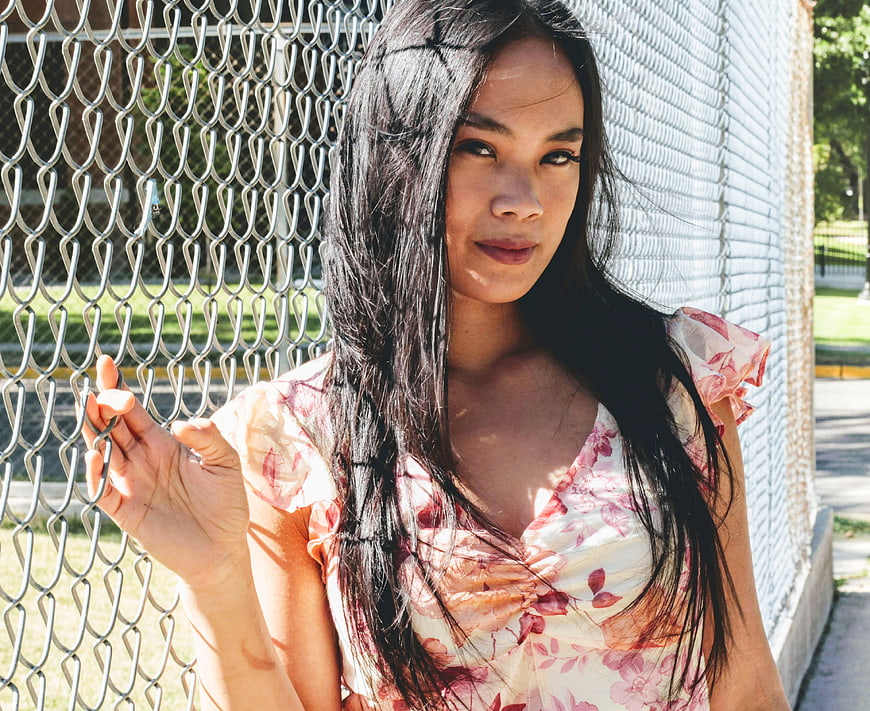 Young Woman in Floral Dress Leaning Against Chain Link Fence