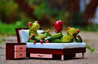 Cute frog figurines relaxing on a miniature bed outdoors
