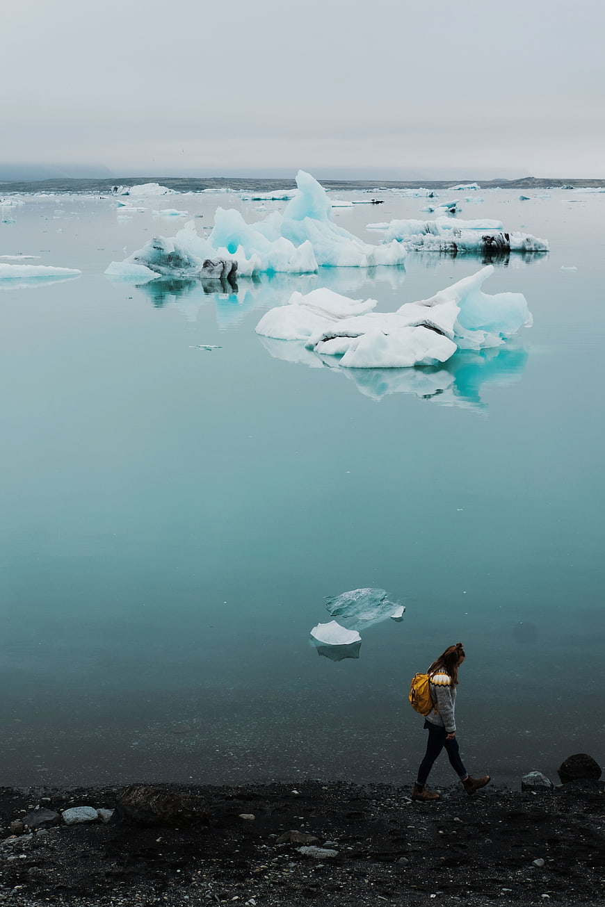 Woman walking on black sand beach near blue icebergs