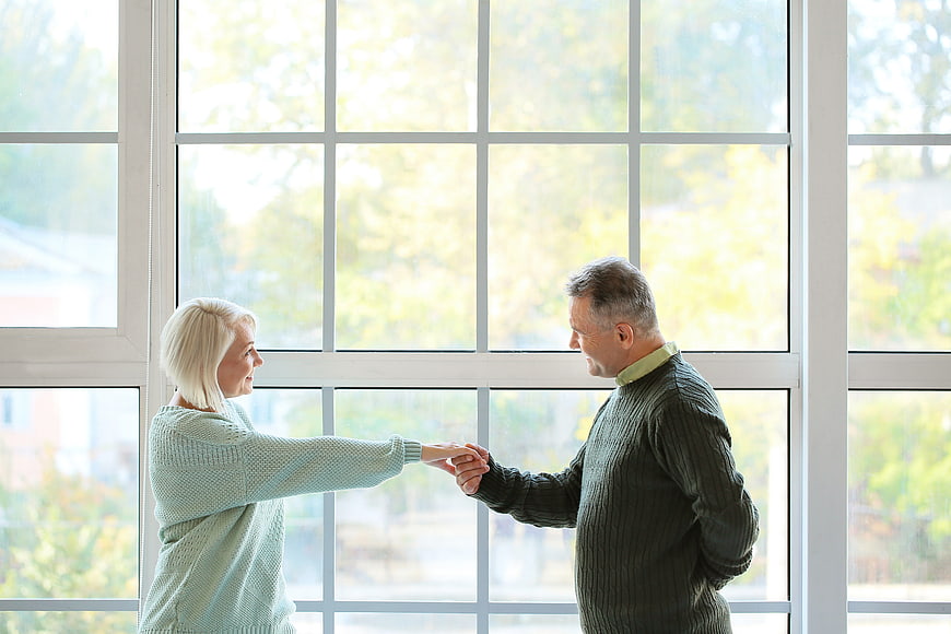 Senior couple dancing playfully in front of large window