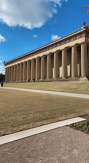 Parthenon replica with columns on grassy hill under blue sky